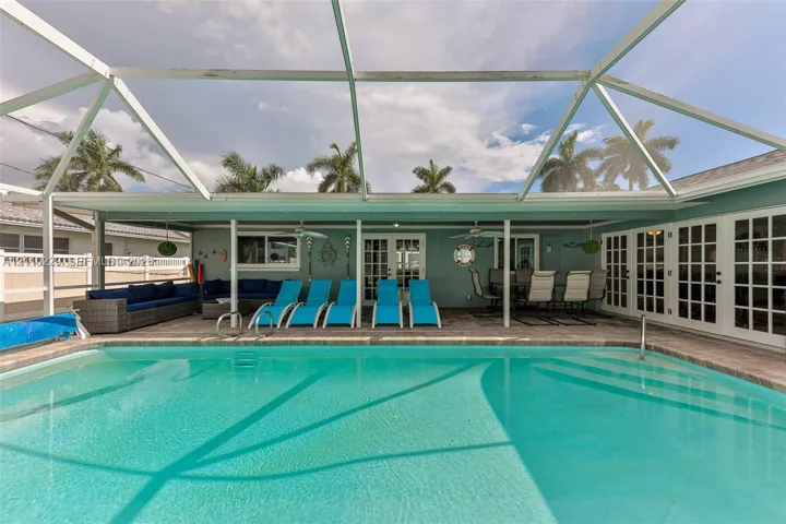 Screen-enclosed pool with paver decking, covered patio area, ceiling fans, and multi-pane glass doors