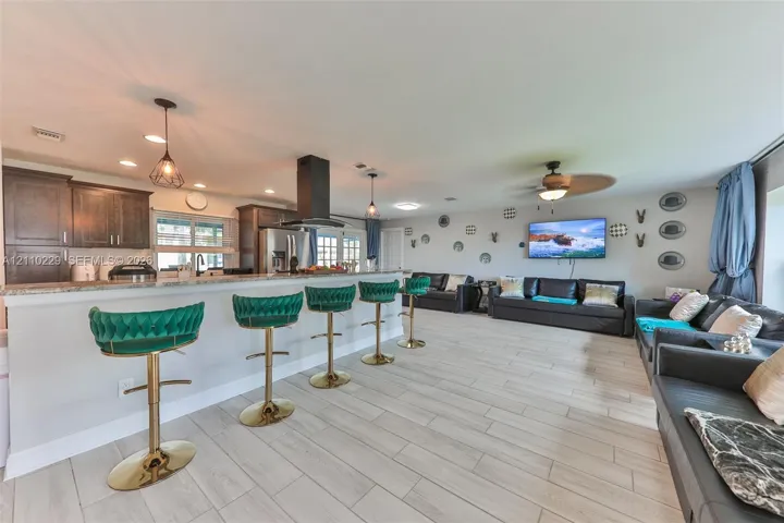 Open-concept interior featuring wood-finish flooring, a kitchen breakfast bar with stone-look countertops, dark-tone cabinetry, a ceiling-mounted range hood, and recessed lighting
