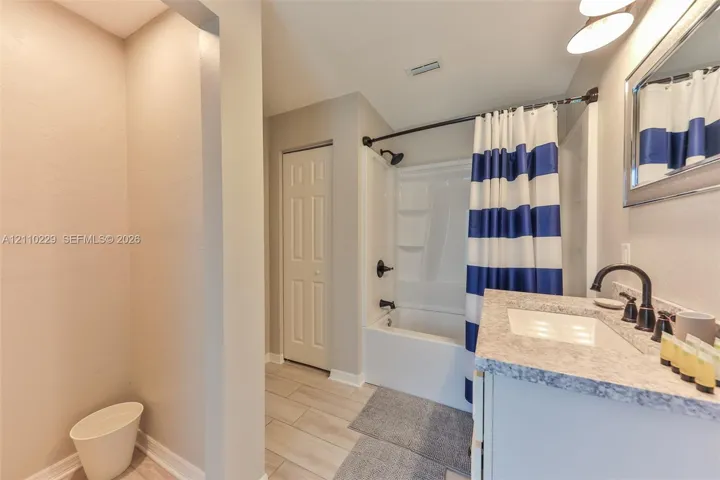 Bathroom featuring a vanity with a stone-finish countertop, undermount sink, matte black faucet, and a combined tub and shower enclosure with a recessed soap shelf
