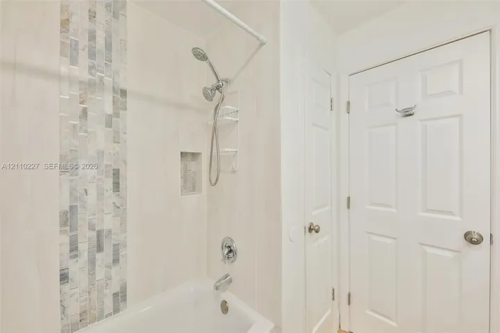 Bathtub and shower combination featuring large-format wall tile, a vertical decorative stone mosaic accent, an integrated wall niche, and polished chrome fixtures