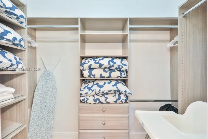 Custom walk-in closet featuring light-toned wood-finish cabinetry, adjustable open shelving, integrated hanging rods, and a three-drawer built-in chest