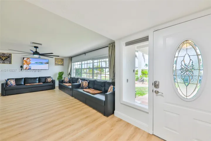 Entrance featuring a white door with an oval decorative glass insert, wood-finish flooring, multi-pane windows, and a black ceiling fan with integrated lighting