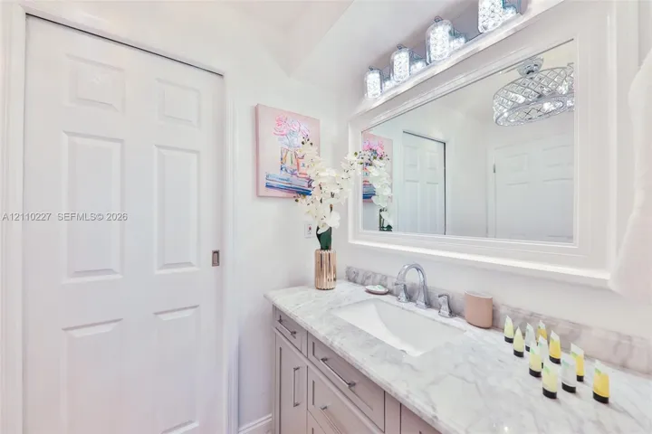 Vanity featuring a stone-look countertop with an integrated rectangular basin, contemporary metallic faucet, recessed cabinetry, and a large, framed mirror with integrated multi-bulb lighting