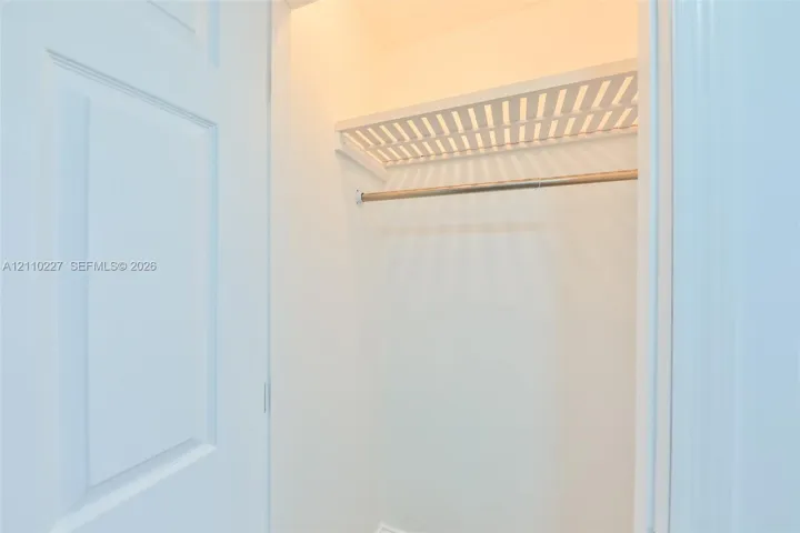 Interior closet featuring a white paneled door, built-in slatted shelving, and a metal hanging rod