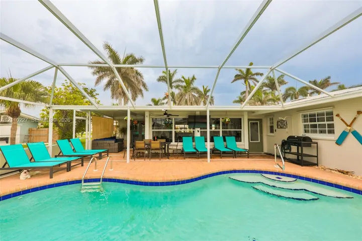 Screen-enclosed patio area featuring a paver deck, built-in swimming pool with step entry, and a ceiling fan