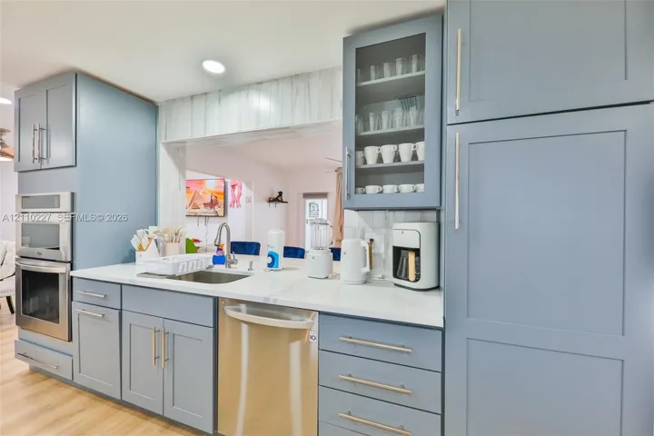 Kitchen featuring blue shaker-style cabinetry, white countertops, stainless steel appliances, and a glass-paneled upper cabinet
