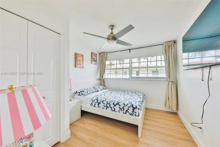 Light-filled room featuring wood-finish flooring, a multi-blade ceiling fan, multi-pane windows, and dual-panel closet doors