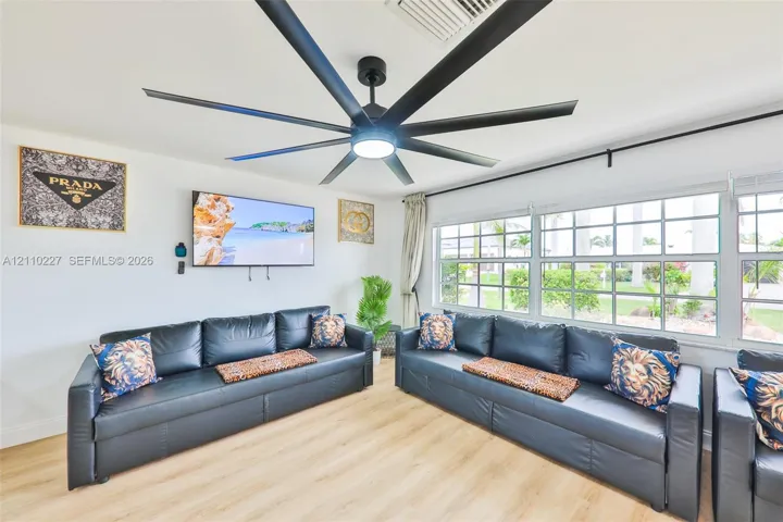 Multi-blade matte black ceiling fan with integrated lighting, wood-finish flooring, and expansive grid-pane windows