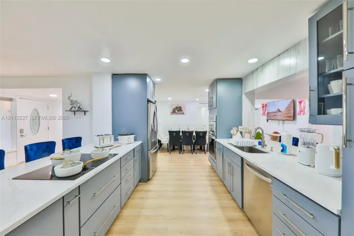 Kitchen featuring light blue cabinetry, stone-finish countertops, stainless steel appliances, a built-in cooktop, and wood-finish flooring