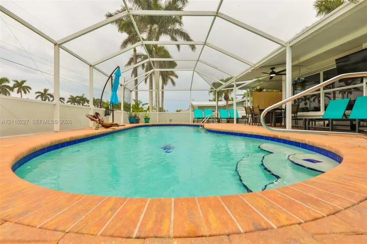 Screened-in outdoor area featuring a swimming pool with built-in steps, brick paver coping, and a covered lanai