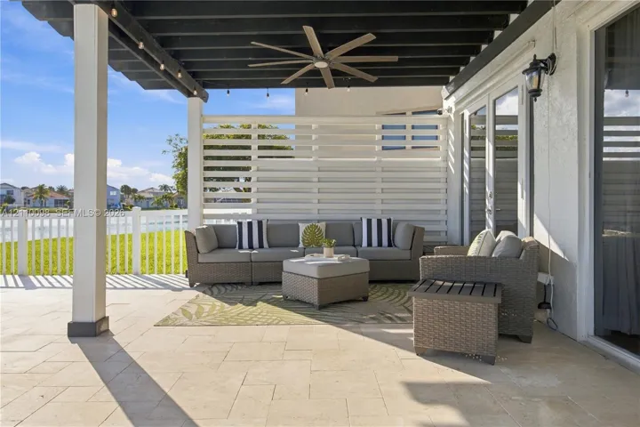 Covered patio featuring stone-tiled flooring, a dark-finished wooden pergola, a ceiling fan, and a white privacy screen