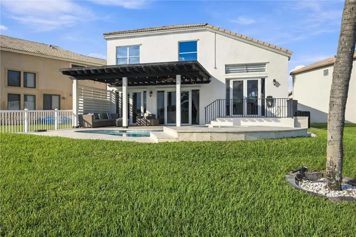 Rear exterior featuring a covered pergola, paver patio, in-ground pool, and white horizontal privacy screening