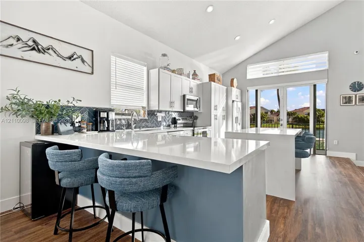 Kitchen featuring a vaulted ceiling, stone-finish countertops, herringbone-patterned tile backsplash, a center island, and wood-finish flooring