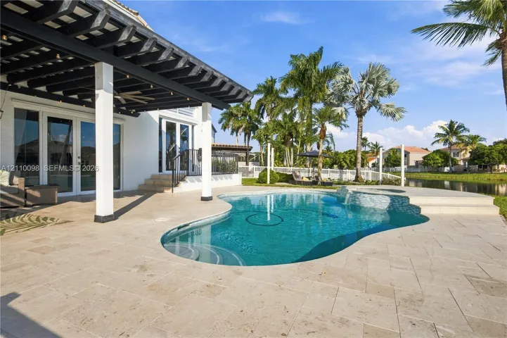 Covered patio featuring a wood-beam pergola, stone-tile decking, freeform swimming pool with a built-in spa, and water frontage