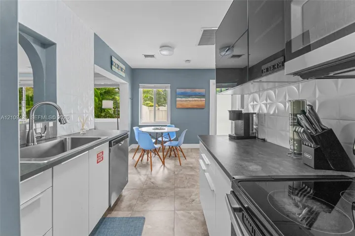 Kitchen featuring high-gloss cabinetry, textured tile backsplash, stainless steel sink with arched faucet, and stone-finish flooring