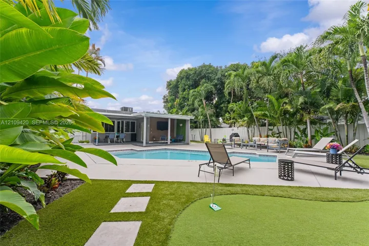 Backyard featuring an in-ground swimming pool, concrete pool deck, synthetic turf putting green, and mature tropical landscaping