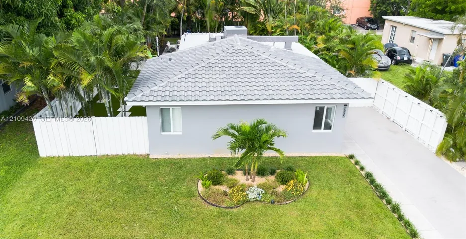 Single-story residence featuring a tile roof, light gray exterior, paved driveway, enclosed side yard, and established landscaping