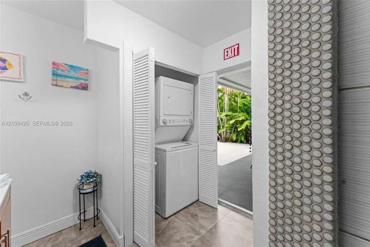 Laundry area featuring stacked appliances, louvered closet doors, and decorative circular tile accents
