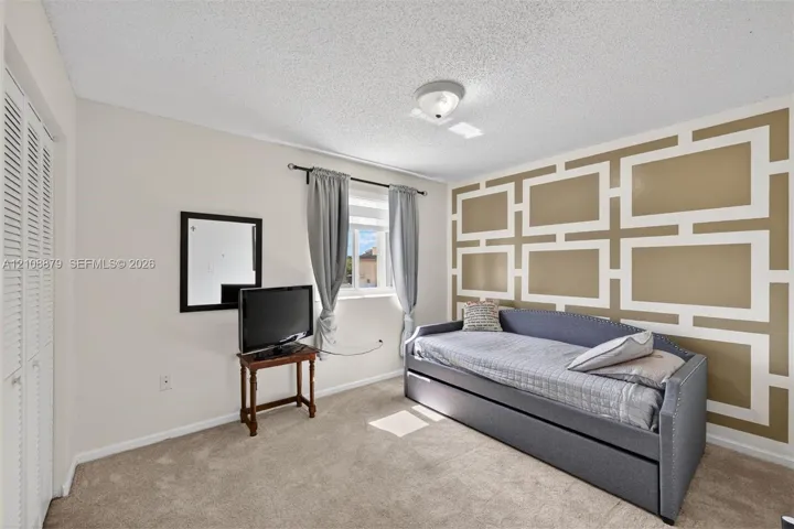Bedroom featuring a geometric accent wall, neutral carpeting, window with a curtain rod, and floor-to-ceiling louvered closet doors