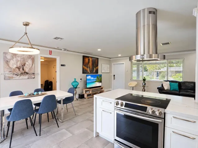 Kitchen featuring white cabinetry, quartz countertops, a stainless steel cylindrical range hood, and a built-in electric cooktop, complemented by neutral tile flooring throughout the area