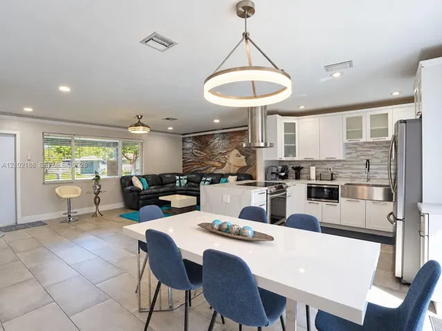 Kitchen featuring white shaker cabinetry, stainless steel apron-front sink, quartz-topped island, modern circular pendant lighting, and neutral large-format floor tiles