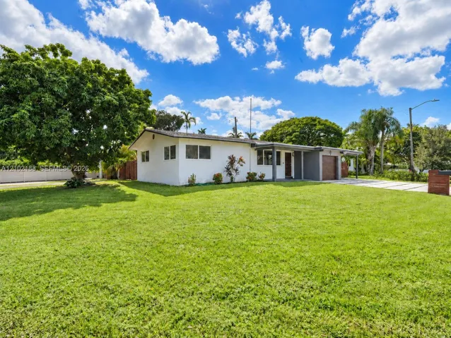 Single-story exterior featuring a painted stucco facade, attached garage, covered entryway, and an expansive lawn with mature landscaping