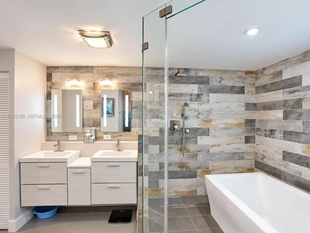 Dual-sink vanity with rectangular basins, integrated LED-lit mirrors, a glass-enclosed walk-in shower, freestanding soaking tub, and multi-toned wood-finish wall tile