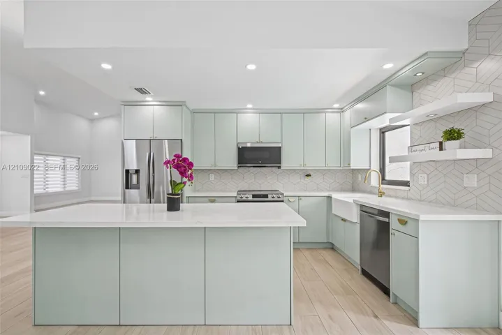 Kitchen featuring light-toned cabinetry, quartz countertops, a central island, geometric tile backsplash, and wood-finish flooring