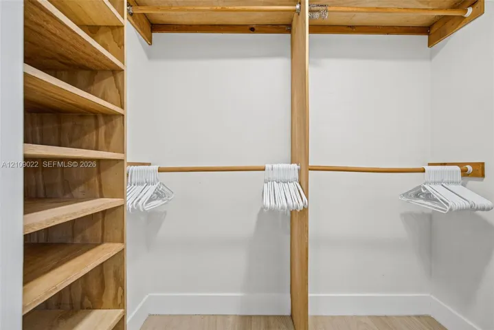 Walk-in closet featuring custom wood shelving units, integrated wooden garment rods, and light-toned wood-finish flooring