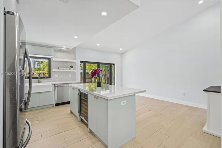 Kitchen featuring a center island with a stone countertop and built-in wine cooler, farmhouse-style sink, geometric tile backsplash with floating shelving, and wood-finish flooring