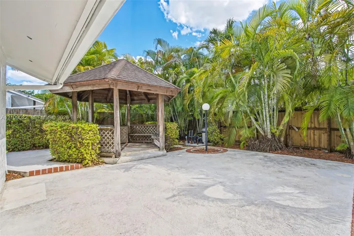 Backyard featuring a wood-frame gazebo with lattice detailing, concrete patio, perimeter wood fencing, and mature palm trees
