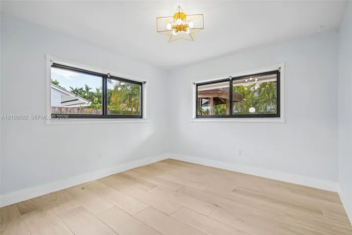 Wood-finish tile flooring, dual windows with black frames, and a geometric gold-tone chandelier