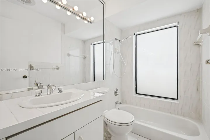 Bathroom featuring a wall-to-wall mirror, built-in vanity with an integrated basin, multi-bulb vanity light fixture, and a tiled shower-tub combination