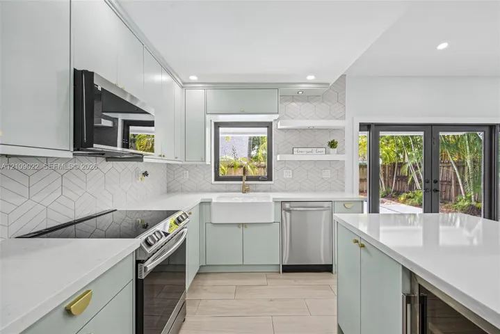 Kitchen featuring soft-toned cabinetry, solid surface countertops, a white farmhouse sink, geometric tile backsplash, and stainless steel appliances