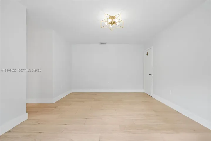 Neutral interior space featuring light-toned wood-finish flooring, a geometric gold-tone chandelier, and a crisp white finish
