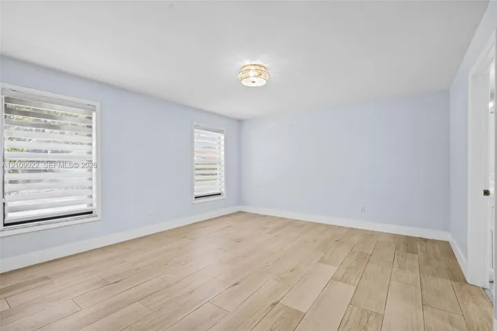 Neutral-toned room featuring wood-finish flooring, two windows with installed adjustable blinds, and a circular flush-mount ceiling light fixture