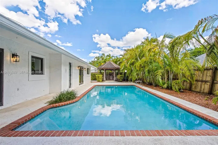 In-ground swimming pool featuring a brick coping surround, paved patio area, and a detached wooden gazebo