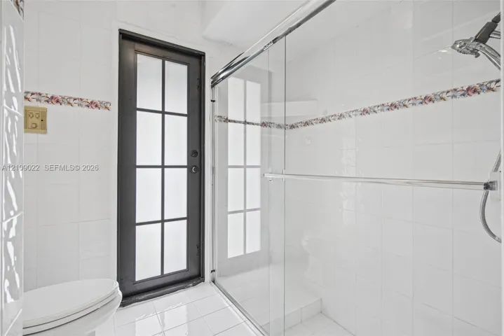 Bathroom featuring white wall tiling with floral inlay accents, a walk-in shower with a sliding glass door, a multi-pane glass-panel exterior door, and white tiled flooring