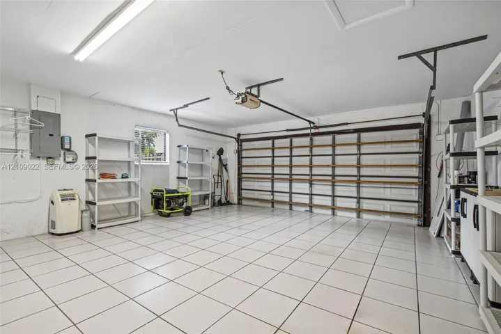 Attached garage featuring white tile flooring, a horizontal paneled door, integrated lighting, and electrical panel
