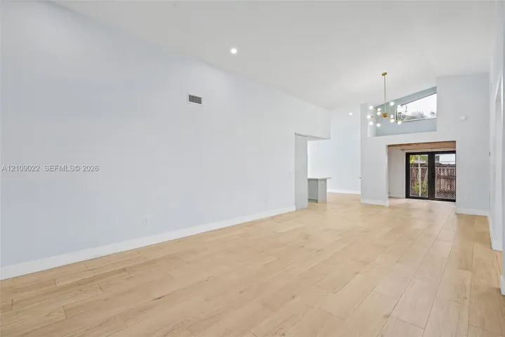 Open-concept interior featuring vaulted ceilings, wood-finish flooring, recessed lighting, a modern multi-arm chandelier, and glass-paneled exterior doors