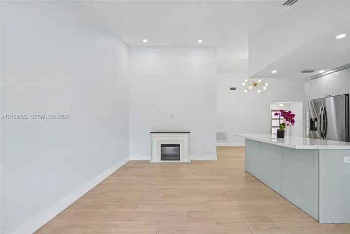 Open-concept interior featuring light wood-finish flooring, recessed lighting, a kitchen island with stone surfacing, stainless steel appliances, and a built-in electric fireplace