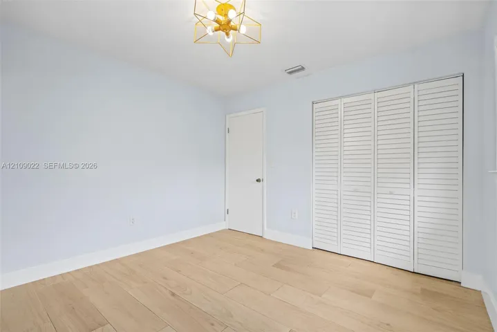 Neutral-toned room featuring wood-finish flooring, a geometric multi-bulb flush-mount light fixture, and a white interior door with a sliding louvered-panel closet