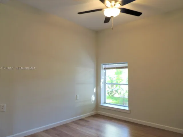 High-ceilinged room featuring wood-finish flooring, a recessed window with deep sill, and an attached ceiling fan with integrated light fixture