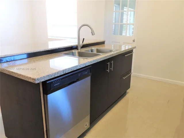 Kitchen island featuring dark cabinetry, stone-surface countertops, stainless steel dishwasher, dual-basin stainless steel sink, and gooseneck faucet