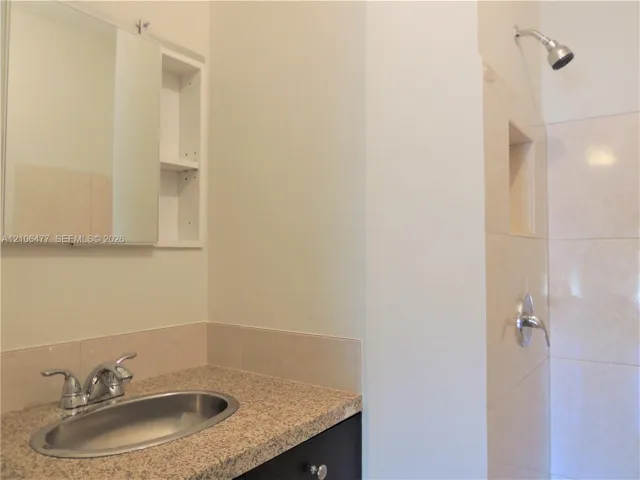 Bathroom featuring a vanity with speckled countertop, oval drop-in sink, dual-handle faucet, integrated medicine cabinet with shelving, and a tiled shower stall with a built-in niche
