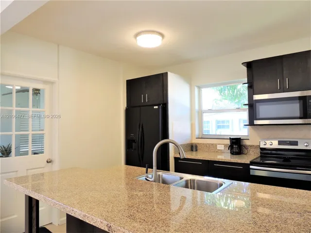 Kitchen featuring dark wood cabinetry, stone countertops, stainless steel double-basin sink with arched faucet, built-in microwave, and multi-lite exterior door