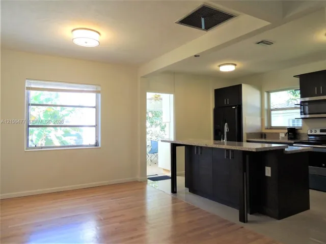 Kitchen featuring dark-finish cabinetry, an island with a stone-style countertop, integrated stainless steel appliances, and wood-finish flooring