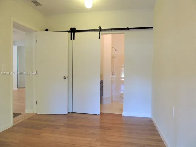 Interior space featuring wood-finish flooring, a white sliding barn door on a matte black track system, and a flush-mount ceiling light fixture