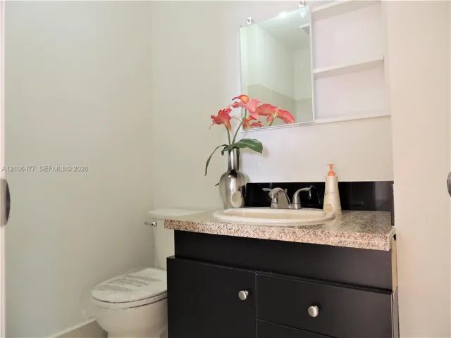 Vanity featuring a dark cabinetry base, stone-finish countertop, integrated sink, and wall-mounted medicine cabinet with integrated shelving