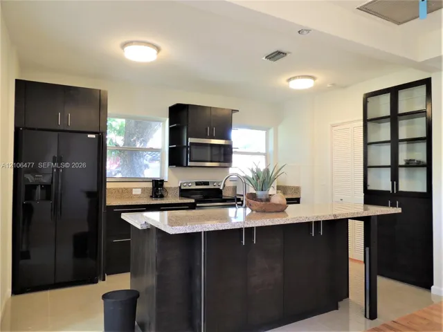 Kitchen featuring dark cabinetry, stone-surface countertops, central island with extended counter seating, stainless steel appliances, and integrated glass-front display cabinetry